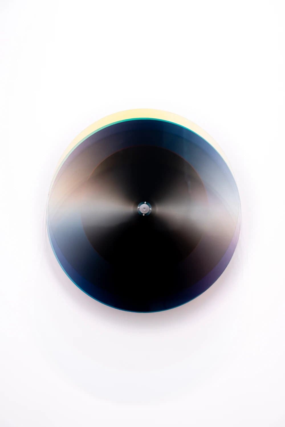Subtractive Variability Kosmos 25: disco cinético de capas translúcidas oscuras sobre eje de aluminio, en la pared del estudio