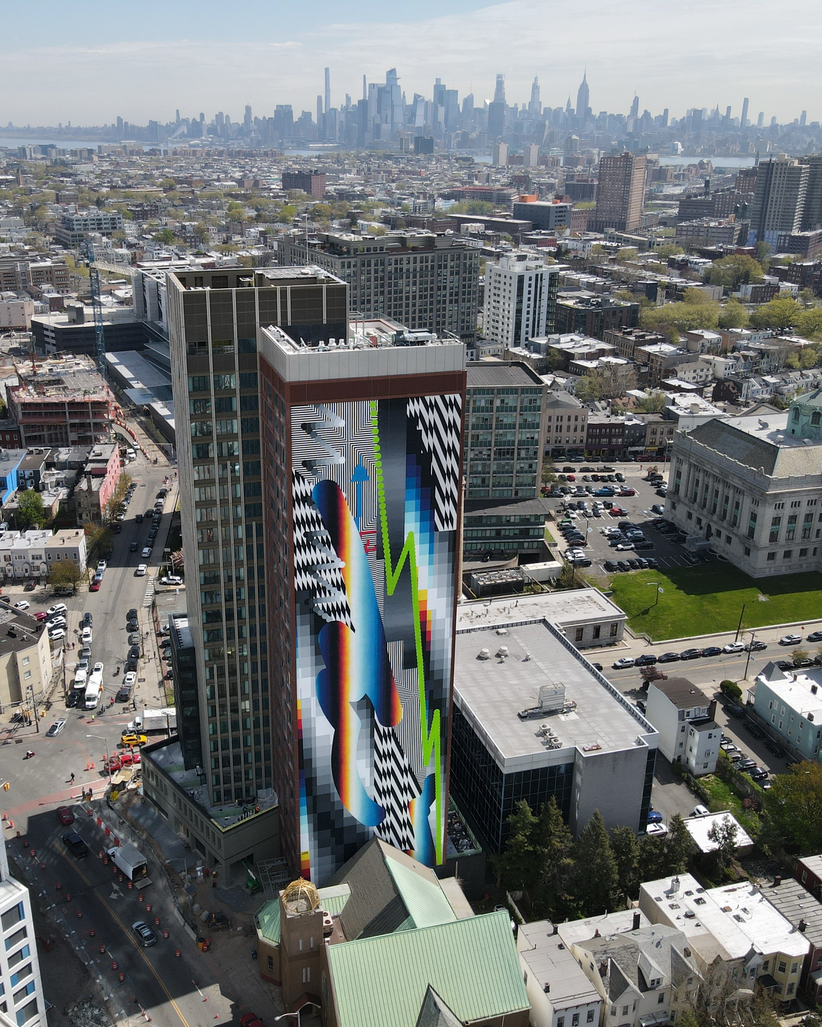 OPTICHROMIE for Jersey City, 2024 — Aérea: la torre con el mural, diminuta contra el skyline — la escala real de la obra.