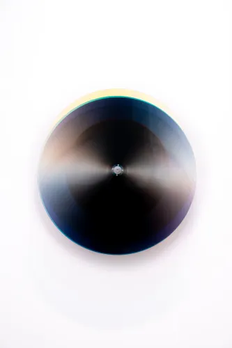 Subtractive Variability Kosmos 25: disco cinético de capas translúcidas oscuras sobre eje de aluminio, en la pared del estudio