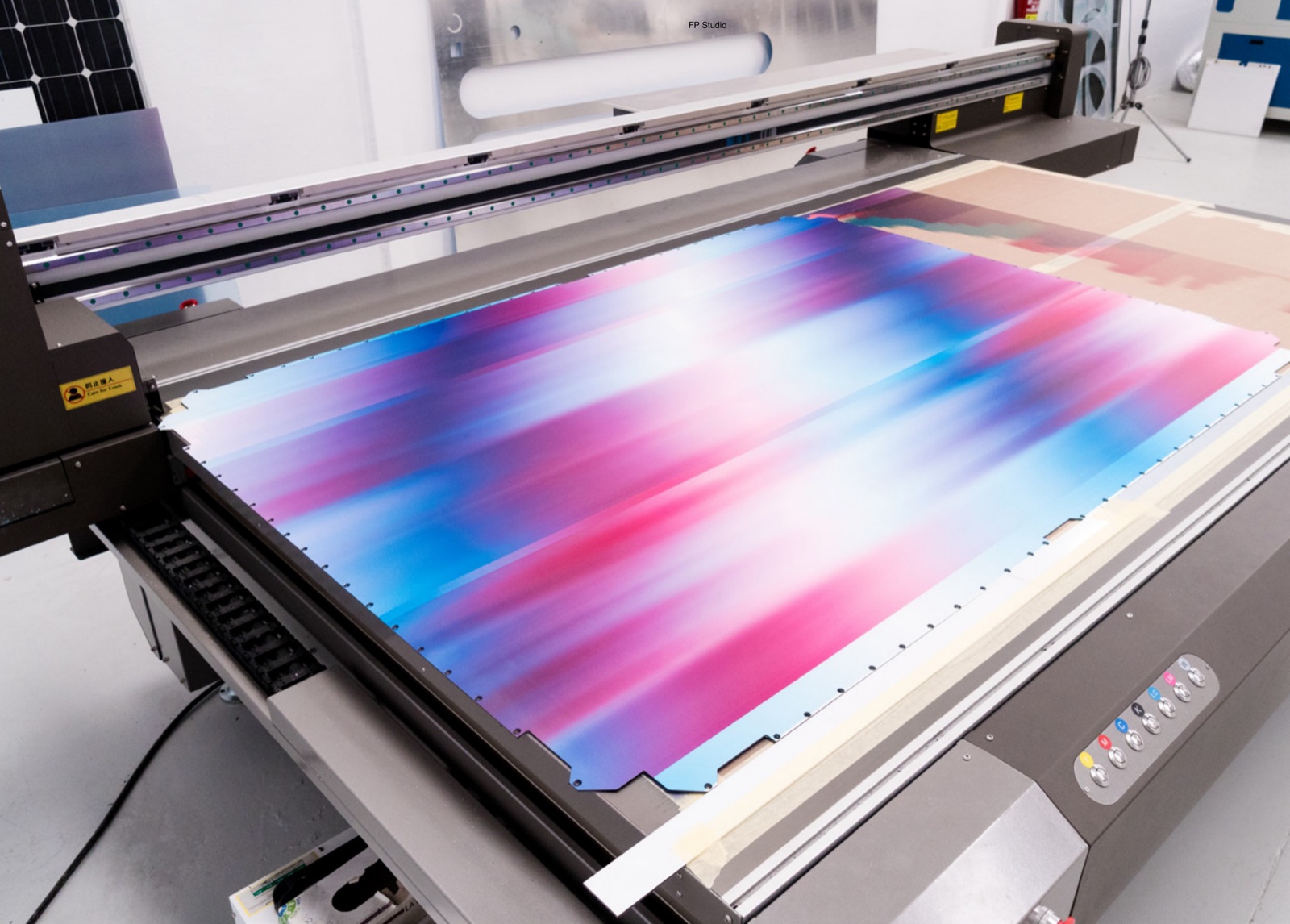 El taller: impresora plana UV de gran formato imprimiendo un degradado sobre panel, FP Studio, Valencia. Desde 2018 las máquinas son propias — la precisión es del equipo.